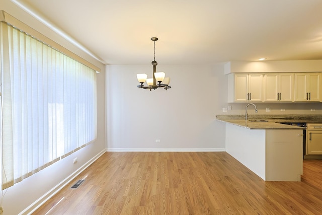 kitchen featuring white cabinetry, a notable chandelier, kitchen peninsula, decorative light fixtures, and light wood-type flooring