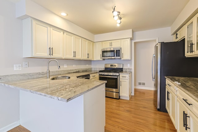 kitchen with sink, light stone counters, kitchen peninsula, appliances with stainless steel finishes, and light wood-type flooring