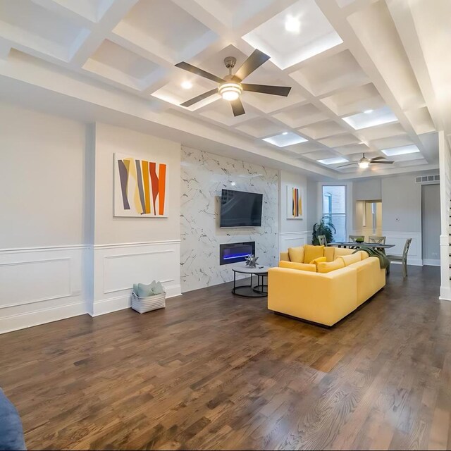 living room featuring a high end fireplace, dark hardwood / wood-style flooring, coffered ceiling, ceiling fan, and beam ceiling