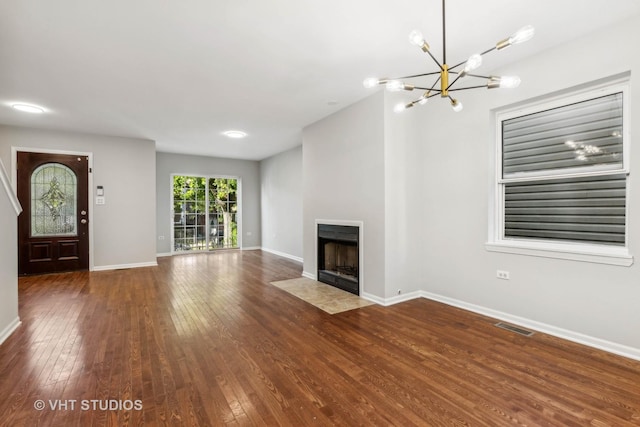 unfurnished living room with a tile fireplace, dark hardwood / wood-style floors, and an inviting chandelier