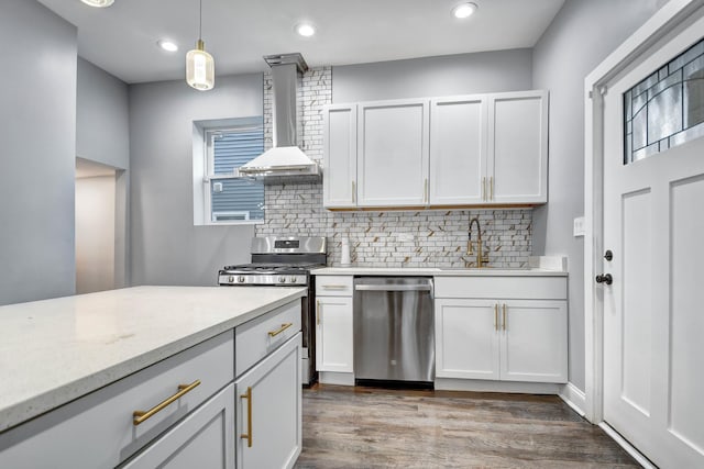 kitchen with pendant lighting, wall chimney exhaust hood, decorative backsplash, white cabinetry, and stainless steel appliances