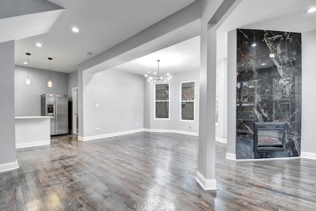 unfurnished living room featuring a high end fireplace, dark wood-type flooring, and a notable chandelier