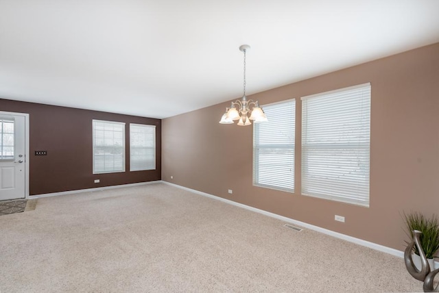 spare room featuring light carpet and an inviting chandelier