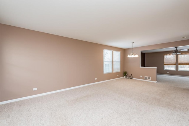 unfurnished room featuring ceiling fan with notable chandelier, light carpet, and a wealth of natural light