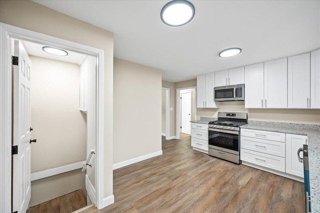 kitchen with hardwood / wood-style floors, stainless steel appliances, white cabinetry, and light stone counters