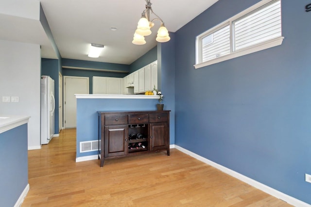 kitchen featuring white refrigerator with ice dispenser, decorative light fixtures, a notable chandelier, white cabinets, and light hardwood / wood-style floors