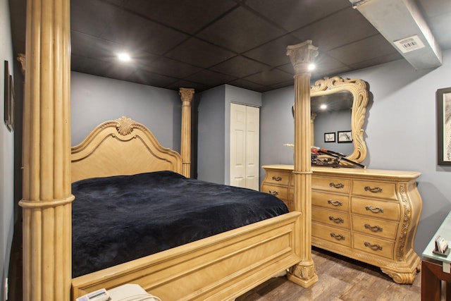 bedroom with wood-type flooring, a drop ceiling, and a closet