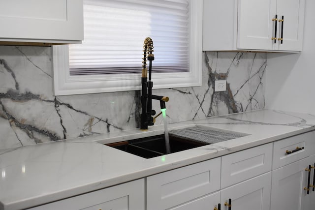 kitchen with decorative backsplash, white cabinetry, light stone countertops, and sink