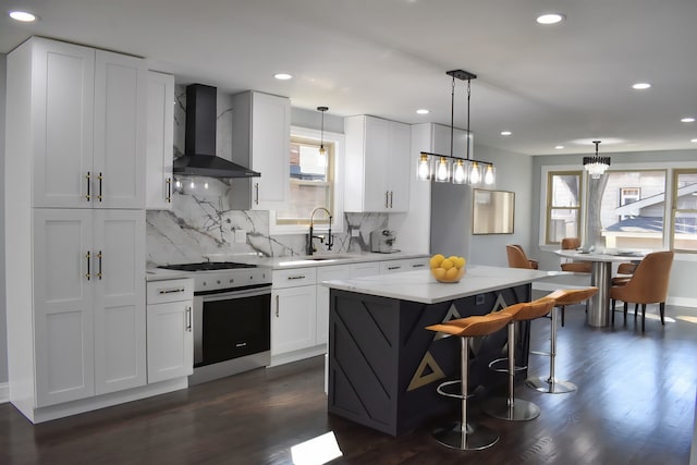 kitchen featuring wall chimney range hood, sink, hanging light fixtures, stainless steel stove, and a kitchen island