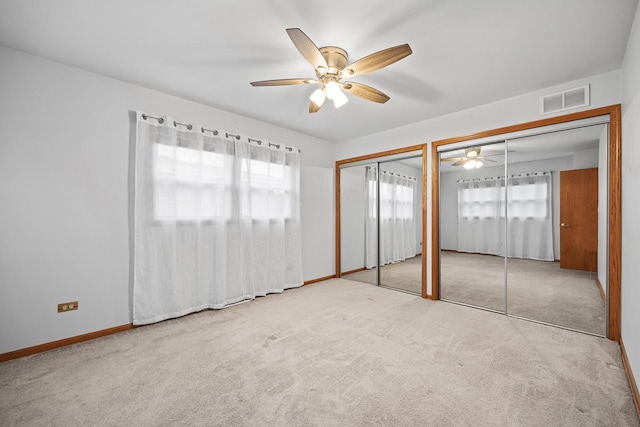 unfurnished bedroom with ceiling fan, light carpet, and two closets