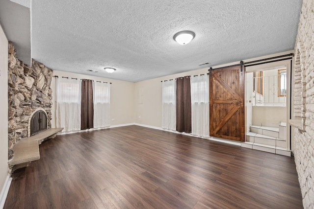 unfurnished living room featuring a textured ceiling, a barn door, wood-type flooring, and a fireplace