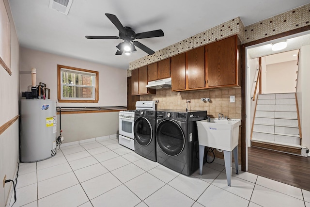 clothes washing area featuring cabinets, brick wall, gas water heater, ceiling fan, and washer and dryer