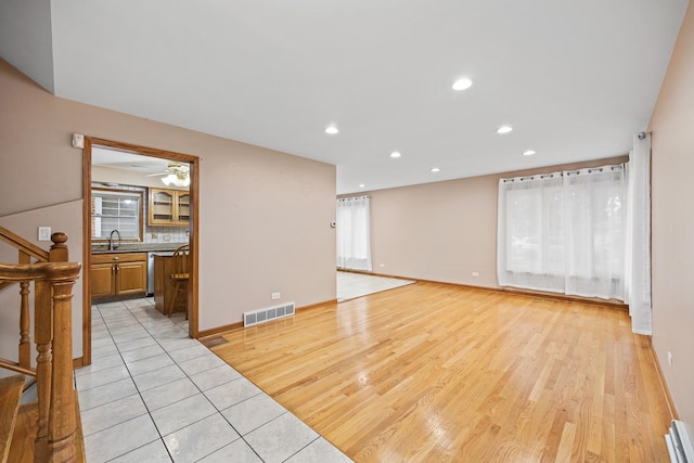 unfurnished living room with light hardwood / wood-style floors, a baseboard radiator, ceiling fan, and sink