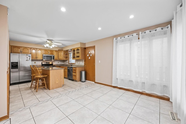 kitchen featuring a kitchen bar, appliances with stainless steel finishes, ceiling fan, light tile patterned floors, and a kitchen island