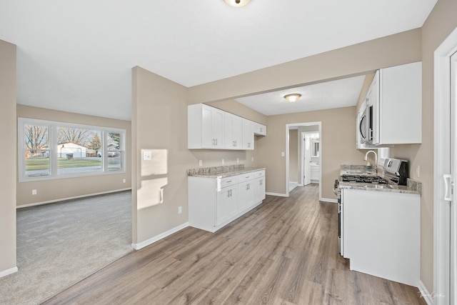 kitchen with white cabinets, light wood-type flooring, light stone counters, and white range with gas cooktop