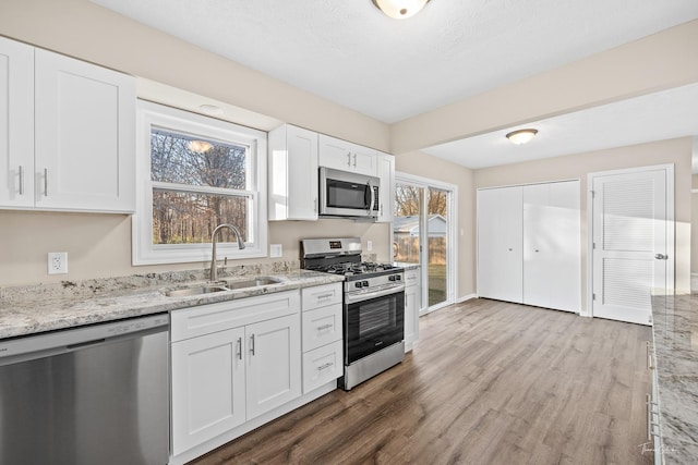 kitchen with light stone countertops, stainless steel appliances, sink, white cabinets, and light hardwood / wood-style floors