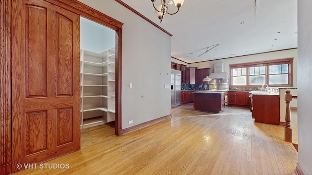 kitchen with wall chimney exhaust hood, light hardwood / wood-style flooring, a kitchen island, ornamental molding, and built in refrigerator