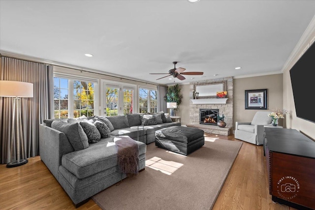 living room with hardwood / wood-style flooring, ornamental molding, a stone fireplace, and ceiling fan