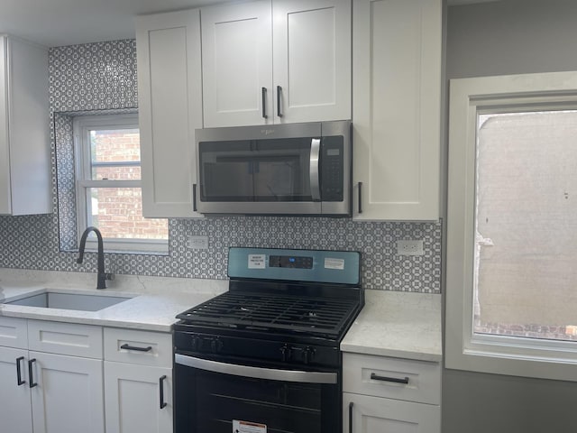 kitchen featuring light stone countertops, sink, white cabinetry, and black gas range oven