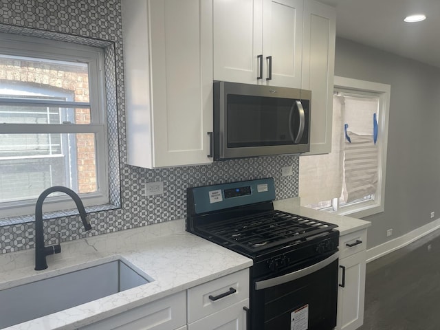 kitchen with black gas range, backsplash, white cabinets, sink, and light stone countertops