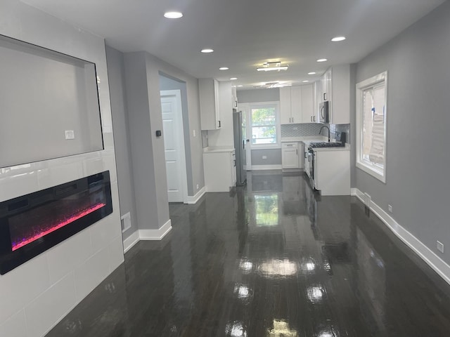 kitchen with white cabinetry, dark hardwood / wood-style floors, a tiled fireplace, decorative backsplash, and appliances with stainless steel finishes