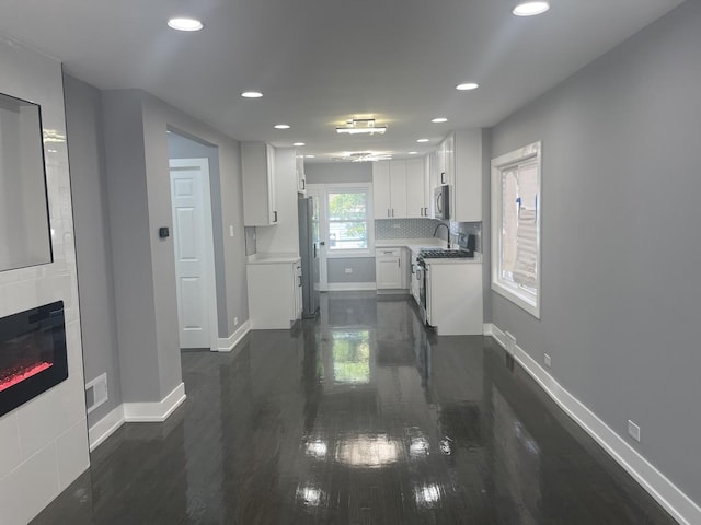 kitchen featuring decorative backsplash, appliances with stainless steel finishes, a tile fireplace, dark hardwood / wood-style floors, and white cabinetry