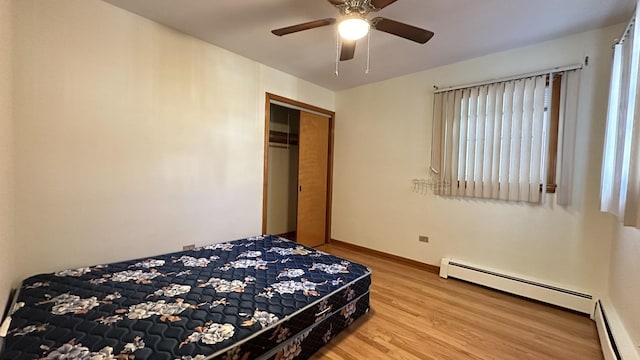 bedroom featuring ceiling fan, a closet, wood-type flooring, and a baseboard heating unit