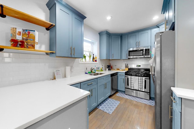 kitchen with sink, light hardwood / wood-style flooring, blue cabinetry, stainless steel appliances, and tasteful backsplash