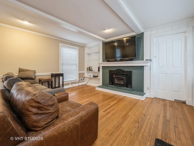 living room featuring ornamental molding, beam ceiling, hardwood / wood-style flooring, built in features, and a wood stove