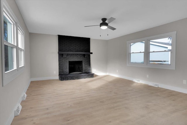 unfurnished living room featuring a fireplace, light wood-type flooring, ceiling fan, and a healthy amount of sunlight