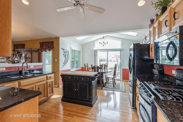 kitchen featuring black appliances, ceiling fan with notable chandelier, sink, vaulted ceiling with skylight, and a kitchen island