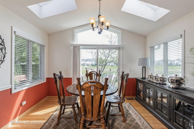 dining area with a chandelier, wood-type flooring, lofted ceiling with skylight, and a healthy amount of sunlight