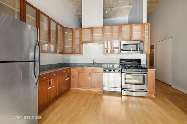 kitchen featuring light wood-type flooring, appliances with stainless steel finishes, dark stone countertops, and sink