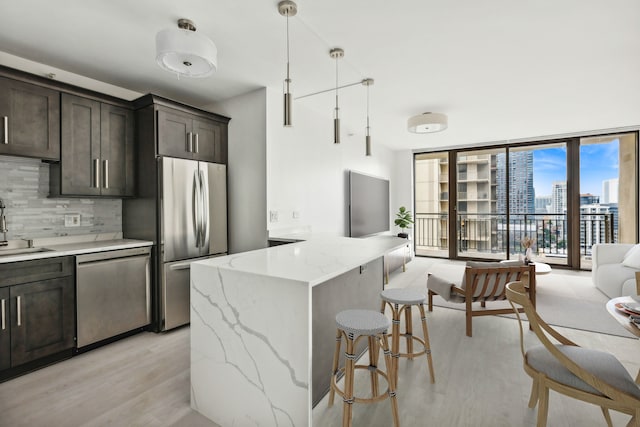 kitchen with light stone countertops, appliances with stainless steel finishes, tasteful backsplash, expansive windows, and pendant lighting