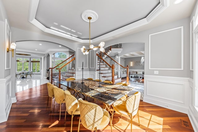 dining space with a raised ceiling, a chandelier, wood-type flooring, and ornamental molding