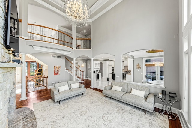 living room with decorative columns, crown molding, wood-type flooring, a chandelier, and a high ceiling