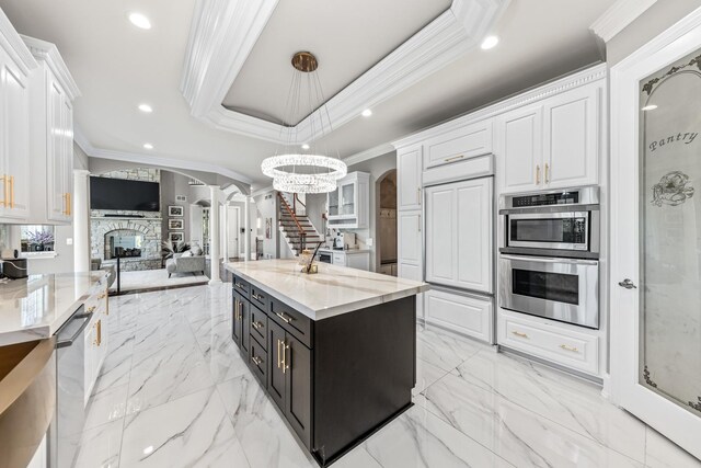 kitchen with decorative light fixtures, an inviting chandelier, a center island with sink, white cabinetry, and a stone fireplace