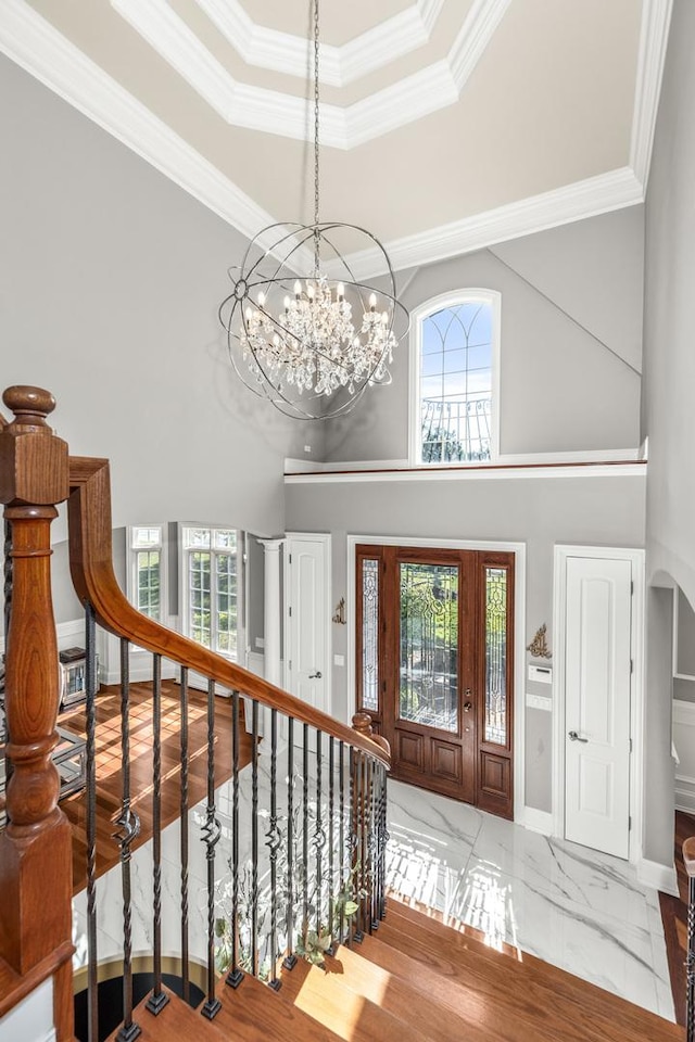 entrance foyer featuring a chandelier, a high ceiling, a tray ceiling, and ornamental molding