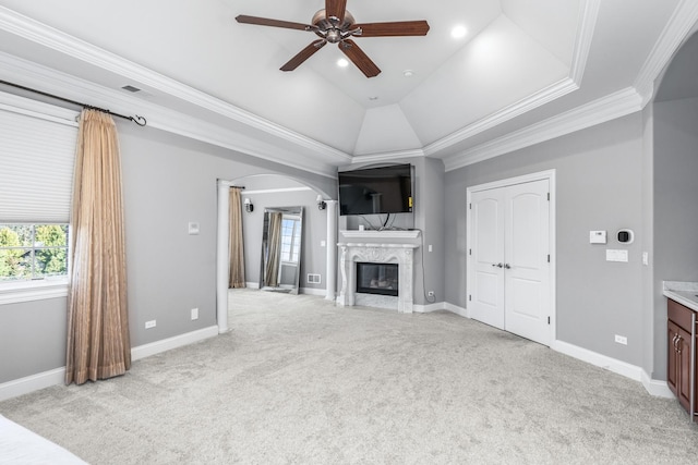 unfurnished living room with crown molding, ceiling fan, a fireplace, a tray ceiling, and light colored carpet