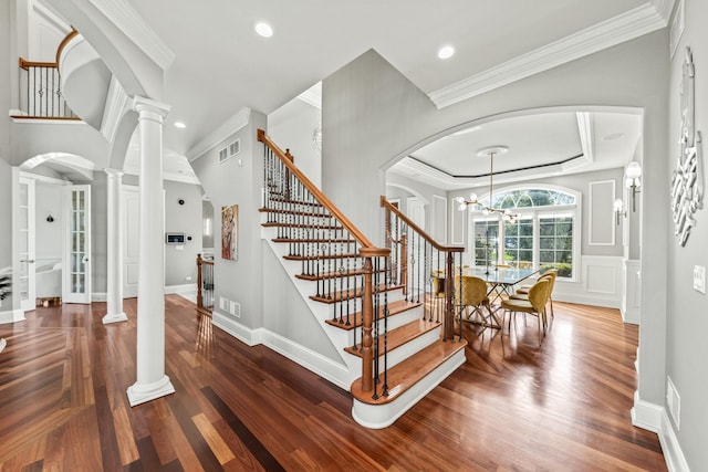 stairs with ornamental molding, a notable chandelier, and hardwood / wood-style floors