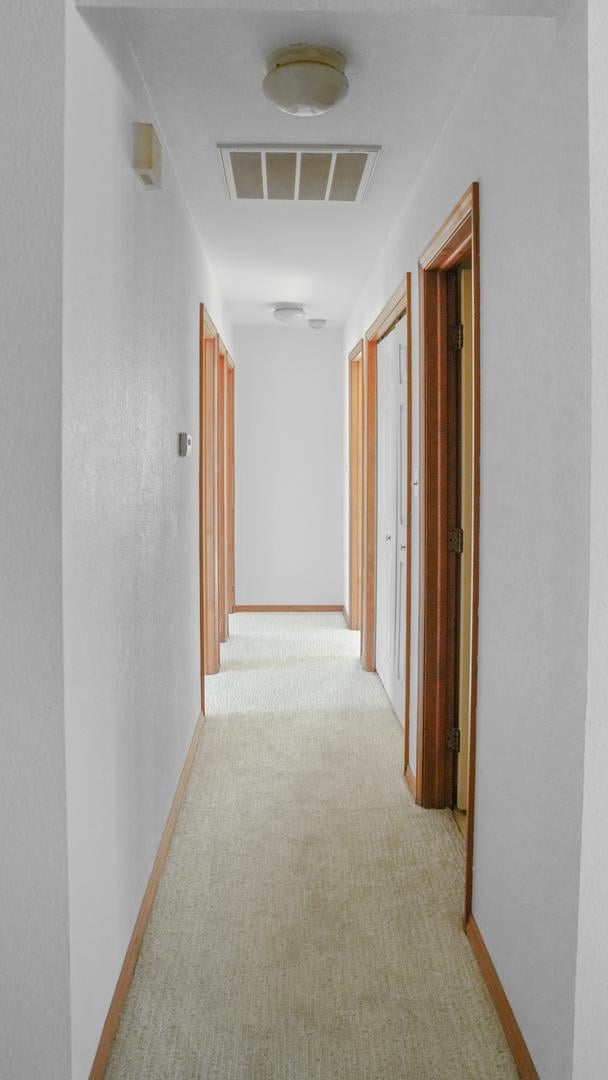 hallway with light carpet, visible vents, and baseboards