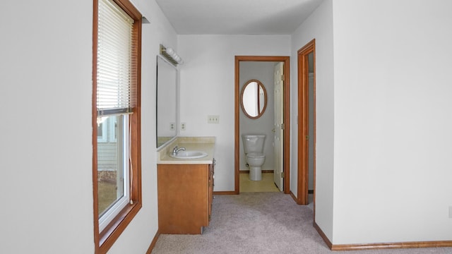 hall featuring baseboards, a sink, and light colored carpet