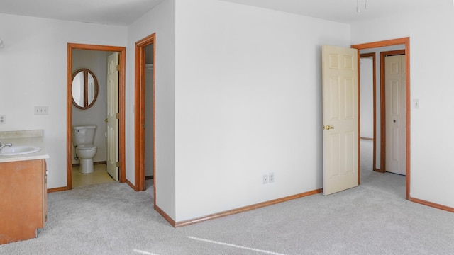 unfurnished bedroom featuring ensuite bath, baseboards, a sink, and light colored carpet