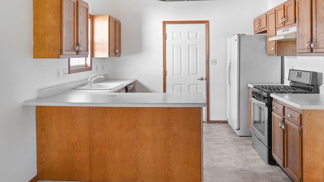 kitchen featuring stainless steel gas range oven, brown cabinets, light countertops, under cabinet range hood, and a sink