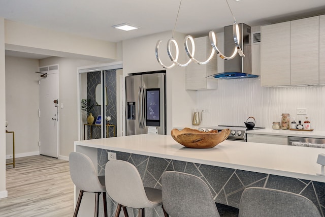 kitchen featuring a kitchen breakfast bar, wall chimney range hood, stainless steel refrigerator with ice dispenser, light hardwood / wood-style flooring, and electric range