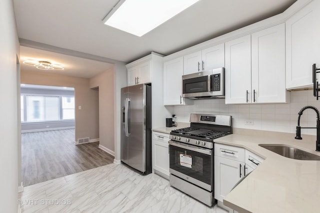 kitchen with sink, white cabinets, backsplash, and appliances with stainless steel finishes