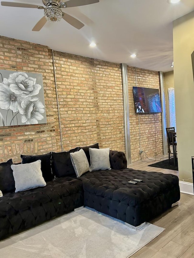 living room featuring hardwood / wood-style flooring, ceiling fan, and brick wall