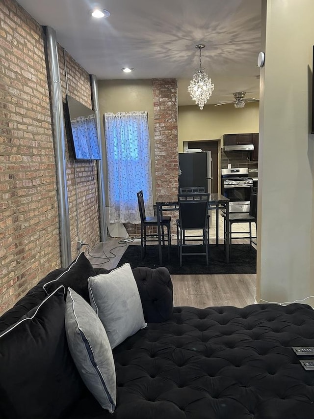 bedroom featuring hardwood / wood-style floors, brick wall, stainless steel refrigerator, and an inviting chandelier