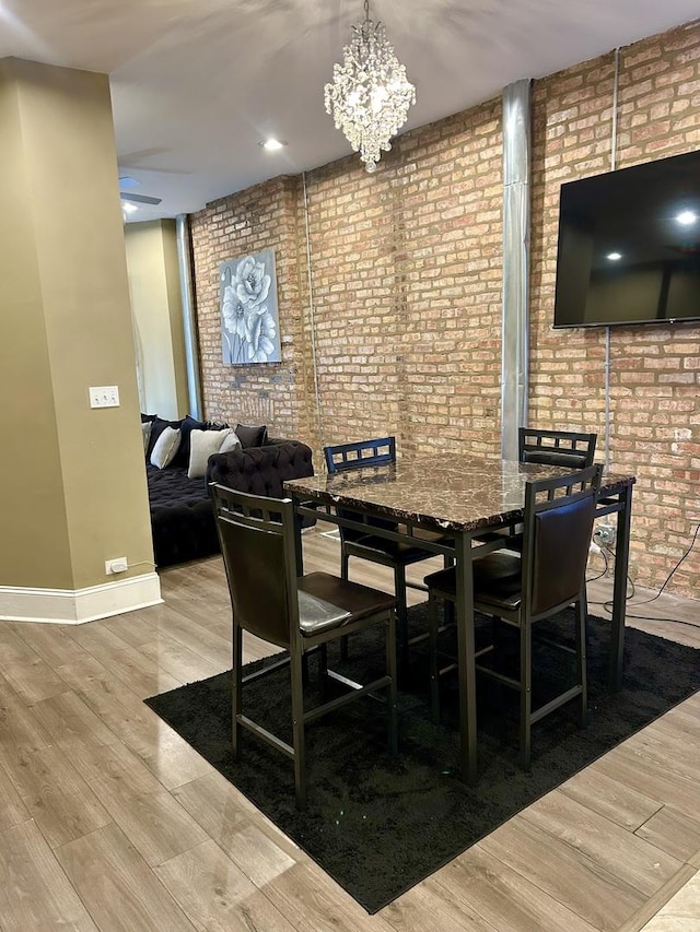 dining area with a notable chandelier, brick wall, and light hardwood / wood-style flooring