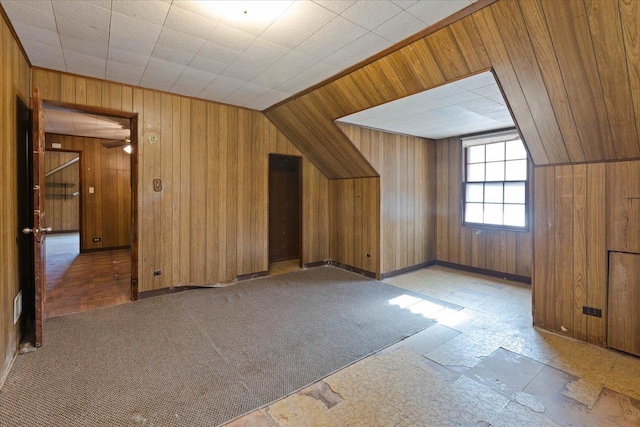 additional living space with wooden walls, ceiling fan, and light colored carpet